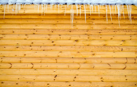 Icicles hanging from roof on log wood wallの写真素材