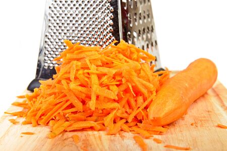 Shredded and whole carrot with metal grater on cutting boardの写真素材