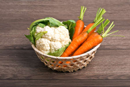 Carrots, cabbage in a wattled basket on a wooden tableの写真素材