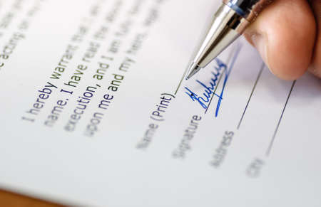 close up of a men hand holding pen and signing papersの写真素材