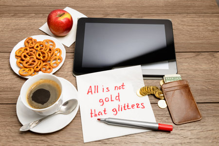 Wooden table with coffee, some food and napkin message proverbAll is not gold that glitters