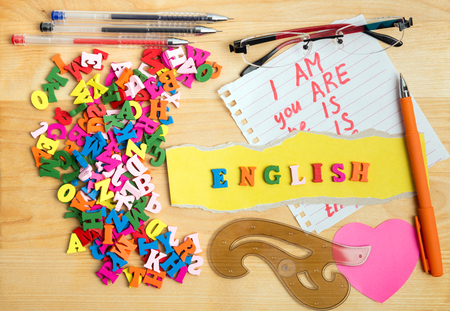 ENGLISH wooden letters and learning stuff near a pile of other letters over wood board backgroundの写真素材