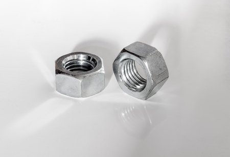 Pair of silver colored metal shiny big screws nuts on white with reflections and shadows