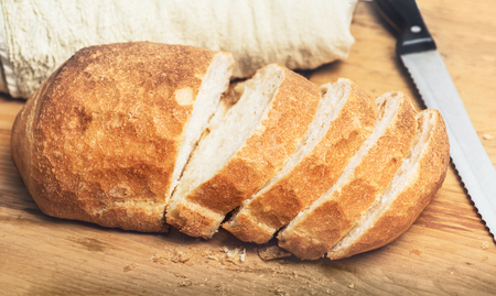 Ciabatta bread loaf slices on wooden board with knife. Fresh crusty white whreat bread italian cuisineの写真素材