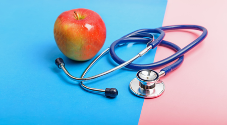 Stethoscope and apple between blue and red areas, the concept of the boundary of health and illness, healthy and unhealthy lifestyle.の写真素材