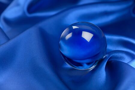 Glass ball on blue silk cloth backgroundの写真素材