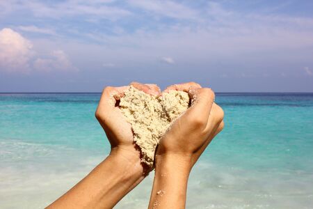 Closeup hands holding white sand heart shape with beautiful beach background