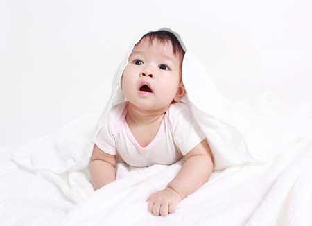 Smiling baby looking at camera under a white blanket/towelの写真素材