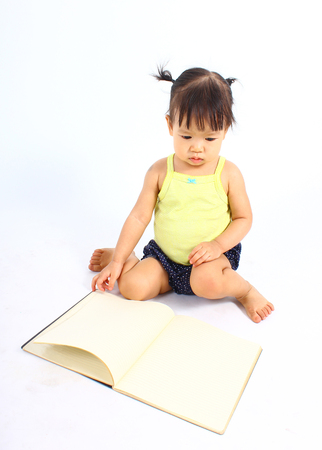 Portrait of little cute baby girl reading book on a white backgroundの写真素材