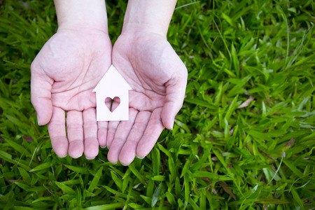 hands holding paper house over green grass.の写真素材