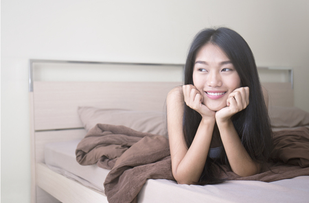 Beautiful young asian woman with attractive smile laying on bed indoors Portrait of woman in bedroomの写真素材