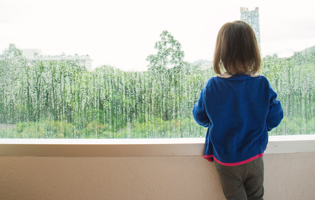 Little girl  looking out of the window with green forest view.の写真素材