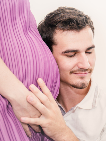 Happy expectant father listening to hear the baby inside his pregnant wife's belly.の写真素材