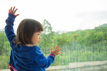 Little girl  looking out of the window with green forest view.の写真素材