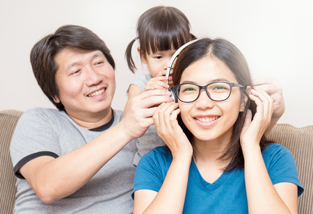 Asian parents and baby girl in sofa using tablet and headphonesの写真素材