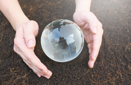 Hands holding earth made from glass over soil backgroundの写真素材