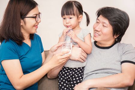 Asian parents giving little daughter a bottle with drink, cute asian family drinking bottle of water.の写真素材