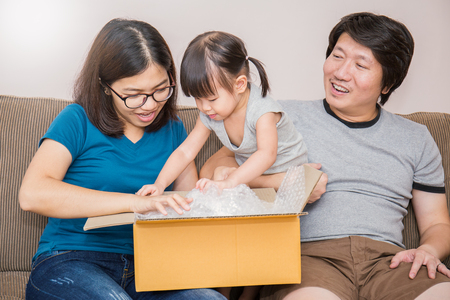 Portrait of asian little girl with her parents unpacking boxes together, asian family moving house unpack the box togetherの写真素材