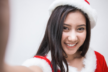 Pretty asian woman wearing santa custume for Christmas time take a self portrait with her smart phone outside, Asian girl selfie,の写真素材