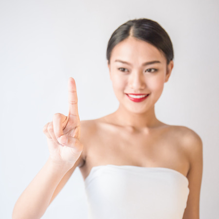 Beauty portrait of young asian woman isolated on white background. Happy beautiful asian tan woman with her index finger point up.の写真素材