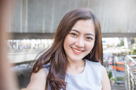 Pretty business woman take a self portrait with her smart phone outside, Asian girl selfieの写真素材