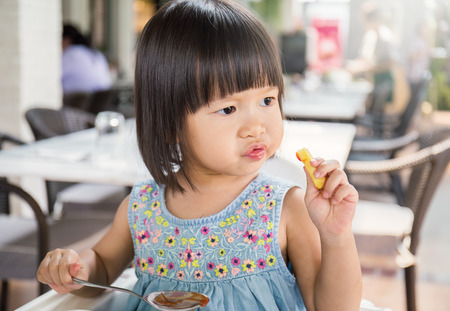 Portrait of little asian girl in fast food restaurant eating fastfood lunch, Happy little asian girl eating a french fries, close upの写真素材