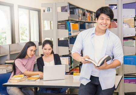 Portrait of asian man with two asian college students using laptop in the library, asian man and woman reading book and study in the library.の写真素材