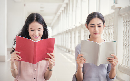 Asian student sitting outside school building reading book, Two asian girls reading book together. Education conceptの写真素材