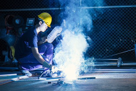 Worker while doing a welding with arc welder with the smoke, man wearing mask with his hands welding...