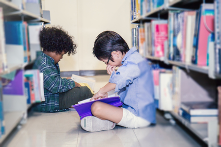 Two boys reading on the library floor. Young students study in the library. Ecucation and back to school concept.の写真素材