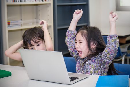 Little boy and girl playing computer games. Small boy and girl tying with laptop in the library. Education home school conceptの写真素材