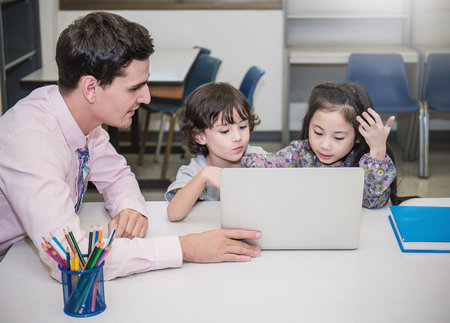 Pupils studying with teacher using computer device in classroomの写真素材