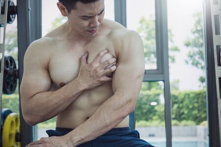 young man his hand on his heart with weight training equipment in sport gymの写真素材