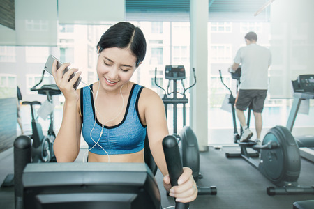 Beautiful sporty asian woman listen to music from smartphone with app running on treadmill, young asian woman with hand holding mobile phone at the gymの写真素材