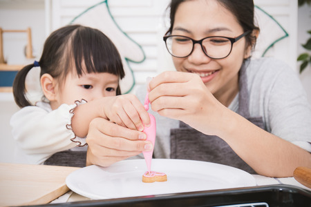 Little asian girl with her brother and her mother baking cake and cookies in the kitchen. Happy family and mother's day conceptの写真素材