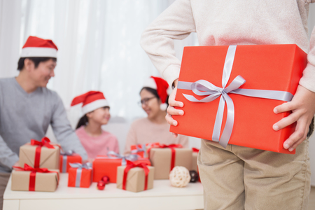 Young boy surprise his family with gift for christmas with red present box behind his backの写真素材