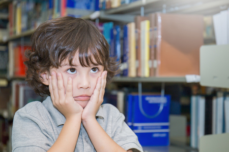 Portrait of little cute caucasian boy in the library. Close up young small caucasian boy feeling bored. Young asian toddler student study in the library. Ecucation and back to school concept.の写真素材