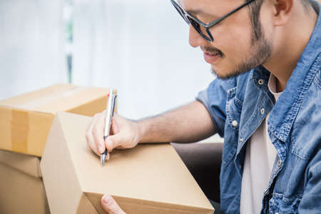 Start up small business entrepreneur SME, asian man writing address on the box. Portrait of young Asian small business owner at home office, online marketing packaging and delivery, SME concept  の写真素材