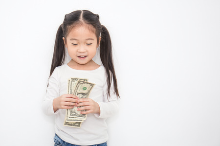 Portrait of cute little asian girl holding money isolated on white background. Small toddler asian girl counting her allowance dollar note.の写真素材