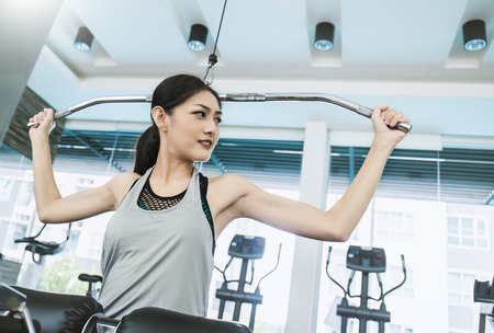 Attractive young asian woman working out with exercise machine at the gym, asian beautiful girl in...