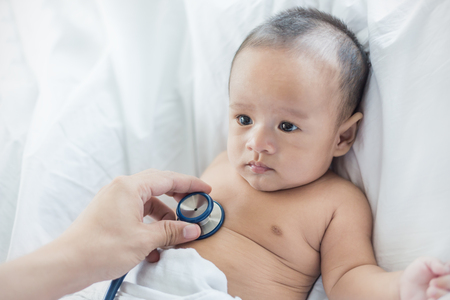 Baby at the doctor getting examine heart beat breath check up with stethoscope. Health care and medical newborn concept.の写真素材