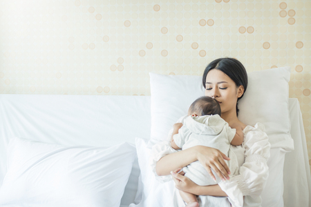 Close up portrait of beautiful young asian mother with newborn baby, copy space with bed in the hospital. Healthcare and medical love lifestyle motherâs day conceptの写真素材
