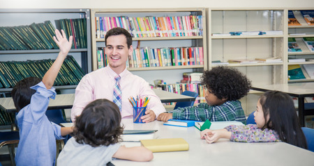Pupils studying with teacher in group study classroom,  Teacher and little children sitting lift their hands up. Young students study ask and answer question in the classroom. Home school back to school concept.の写真素材