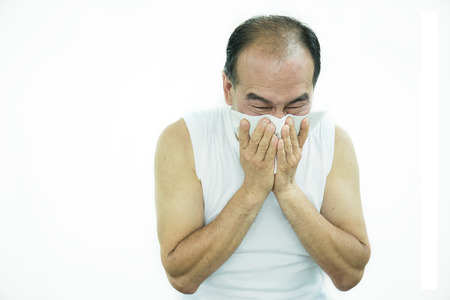 Senior old man with a cold blowing his runny nose with tissue. Portrait of Asian senior man get sick sneezing from flu isolated on white background. Healthcare and medical concept.の写真素材