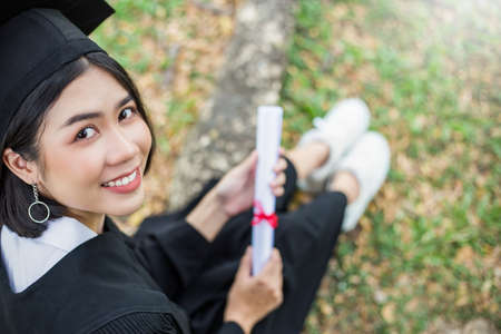 Close up portrait of young asian woman outside the building on her graduated day. Cute asian girl with her hands holding certificate paper, Education success graduate concept bannerの写真素材
