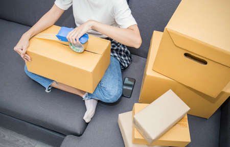 Young asian woman taping up a cardboard box in home office SME e-commerce business, relocation and new small business concept, SME conceptの写真素材