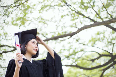 Portrait of young asian woman look up outside the building on her graduated day. Cute asian girl with her hands holding certificate paper, Education success graduate with copy space concept bannerの写真素材