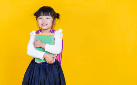 Portrait of young little asian girl hand holding books bag backpack isolated on yellow background...