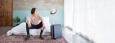Portrait of young asian man traveler prepare suitcase for holiday vacation. Top overhead view of tourist man lying on bed in hotel room. Asian backpacker travel lifestyle concept bannerの写真素材