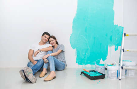 Portrait of happy smiling asian couple renovating painting wall house. Mother father repairing paint...